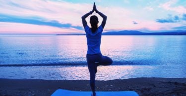 Mulher fazendo posição de Yoga em frente ao mar.