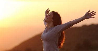 Mulher de braços aberto e sorrindo em campo aberto com a luz do pôr do sol