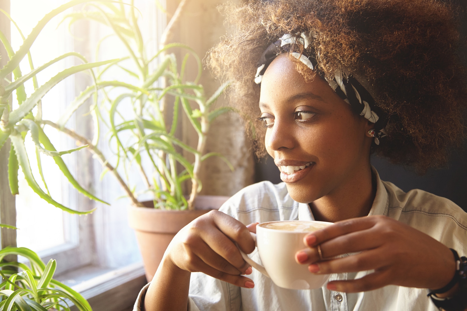 People and leisure. African woman dressed in trendy clothes holding cup of coffee or tea enjoying hot drink. Black student girl having rest at cafe after college drinking cappuccino looking relaxed