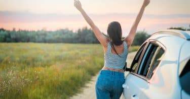 Mulher encostado no carro com os braços para cima