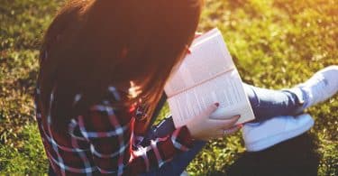 Mulher sentada na grama lendo livro.