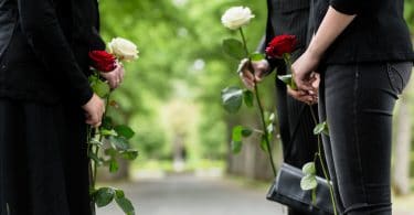 Pessoas vestidas de preto, em um cemitério, segurando rosas vermelhas e brancas.