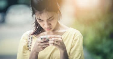 Menina asiática mexendo no celular com cara de séria.