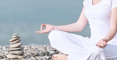 mão de uma mulher meditando em uma pose de ioga na praia