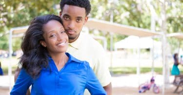 Casal hétero negro posando para foto abraçados com paisagem de parque ao fundo.