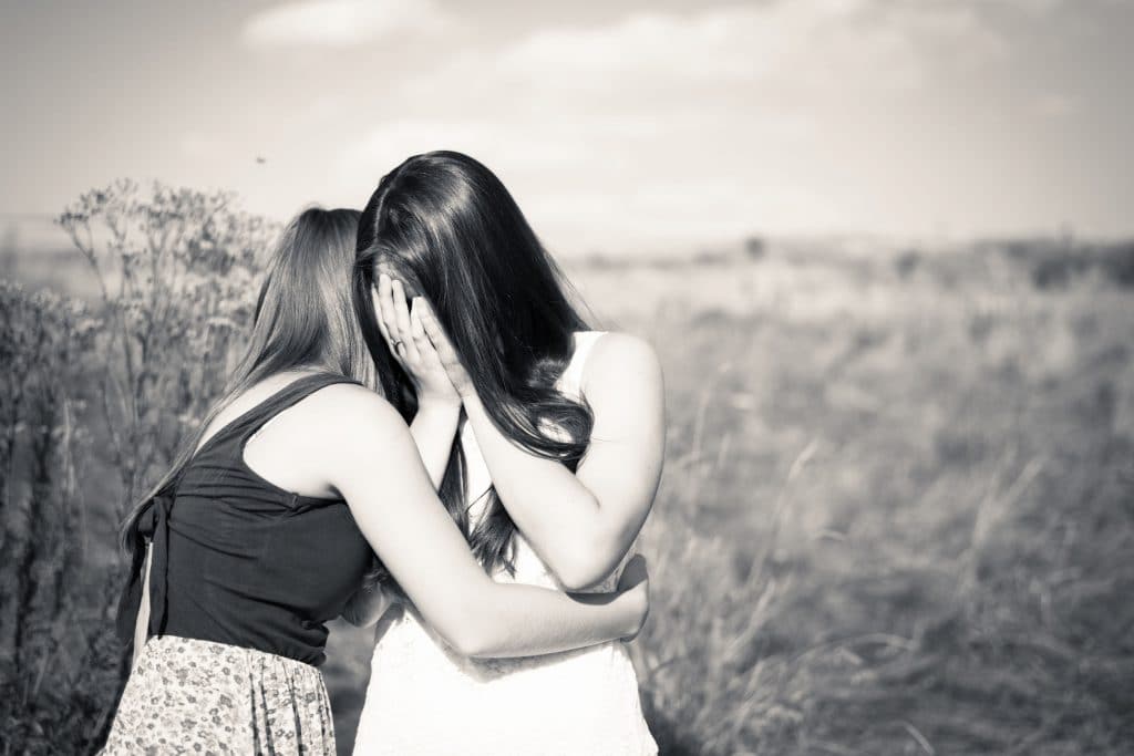 Foto preta e branca de duas adolescentes se abraçando, uma delas esta chorando enquanto a outra tenta conforta-la.