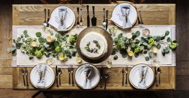 Mesa pratos postos e bolo no meio. Decoração de folhas e flores.