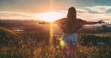 Menina em montanha com os braços abertos. Fundo de pôr-do-sol.