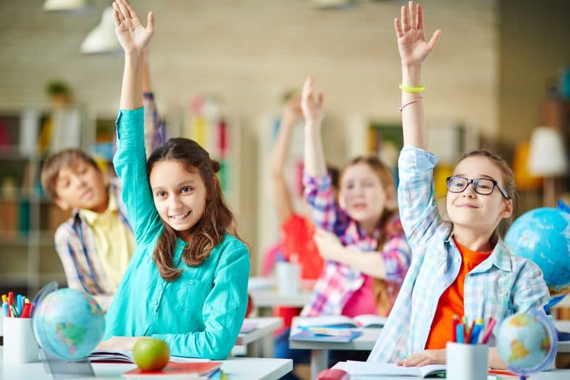 Crianças na sala de aula levantando a mão com sorriso no rosto