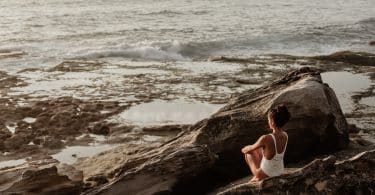 Mulher sentada em uma rocha olhando o mar