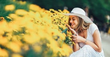 Mulher jovem sorrindo ao lado de um canteiro de flores amarelas.