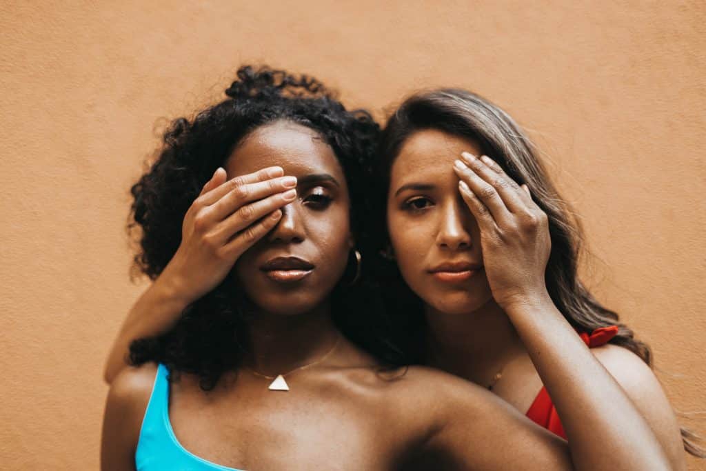 Duas mulheres com as mãos nos olhos uma da outra