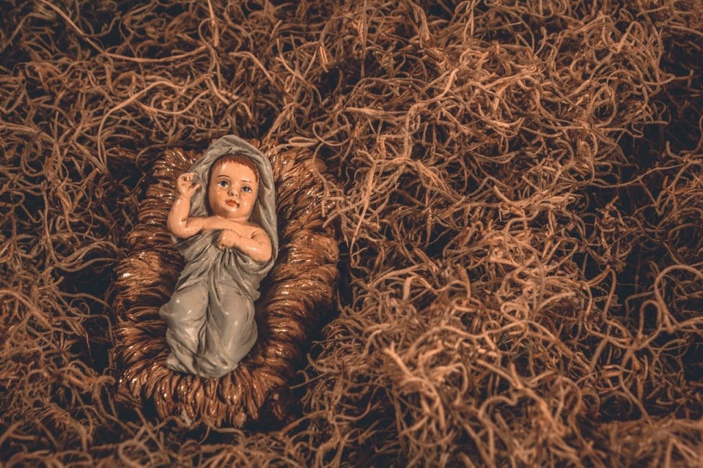 Boneco em miniatura de Jesus quando bebê, enrolado em um tecido azul, sobre montes de feno.