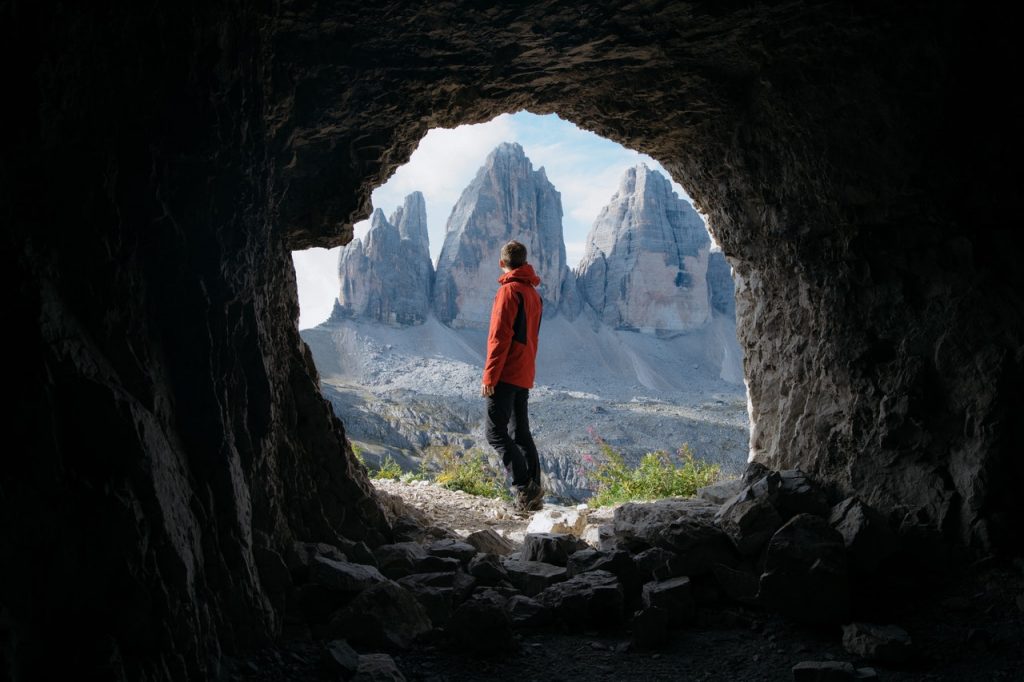 Homem de costas visto de caverna com paisagem ao fundo