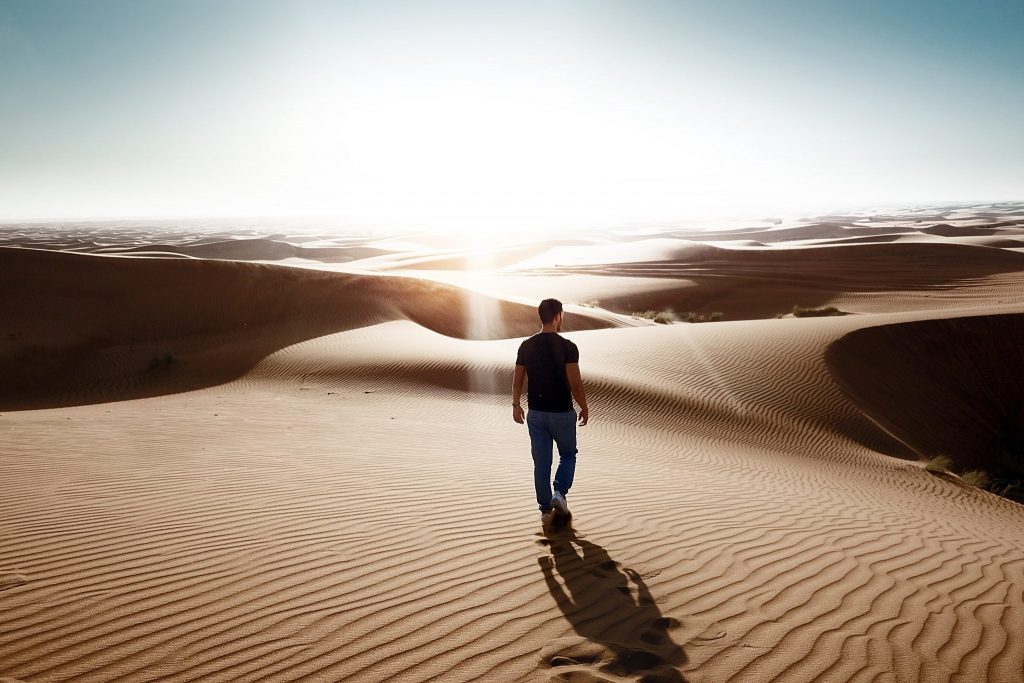 Homem de costas caminhando em deserto de areia