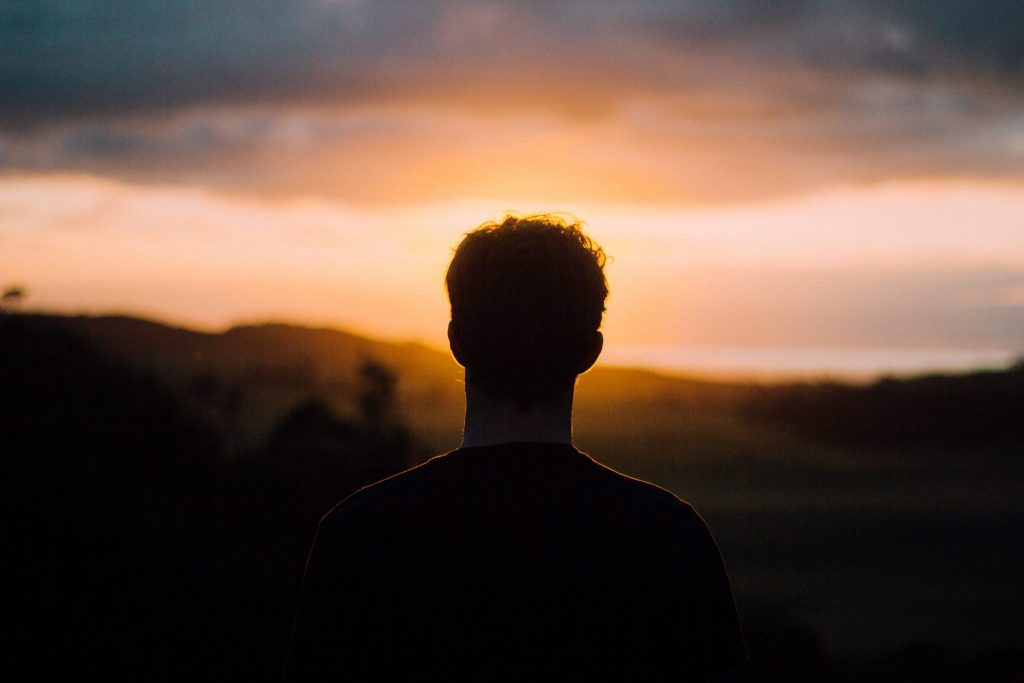 Homem de costas olhando pôr-do-sol
