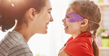 Mãe arrumando capa de super-herói da filha que está sorrindo