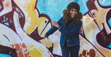 Mulher sorrindo com os olhos fechados de frente para um muro colorido