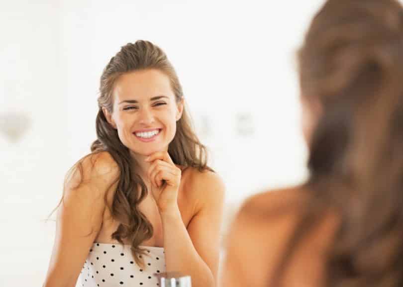 Mulher sorrindo enquanto olha seu reflexo no espelho
