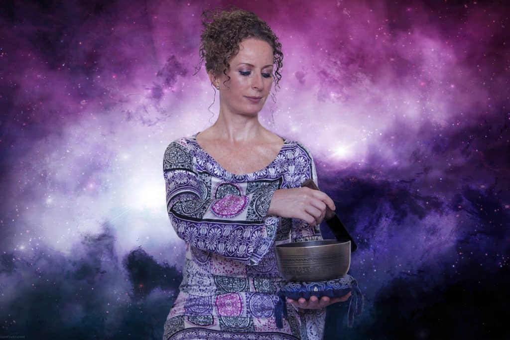 Mulher preparando uma base para o uso durante a aplicação do Reiki. Ela usa um vestido com desenhos abstratos. Ao fundo um painel parecendo a imagem do universo nas cores roxo, lilás e branco.
