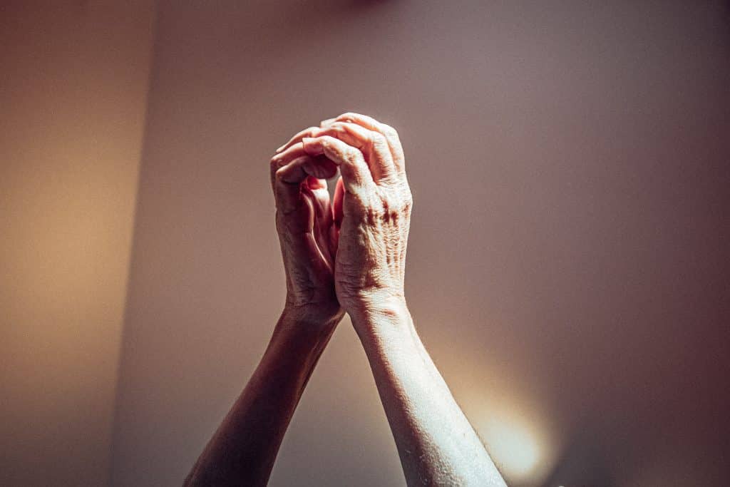 Mãos de uma pessoa com as palmas unidas para cima, em sinal de oração.