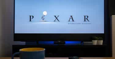 Televisão mostrando a animação da Pixar e na mesa em frente uma xícara e um controle da TV