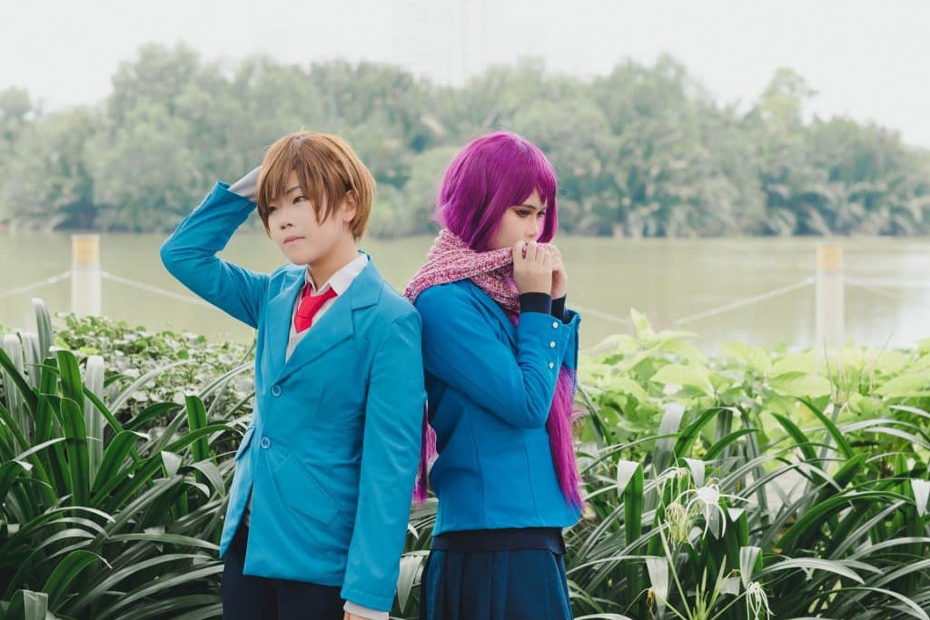 Imagem de um jovem asal oriental em um jardim. Ela usa um cabelo roxo e ele um cabelo avermelhado. Ambos vestem um ter o azul, um uniforme escolar.