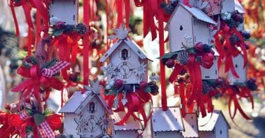 Imagem de várias casinhas de pássaros feita de madeira e pintadas na cor branca e enfeitadas com fitas vermelhas e outros adornos de natal.