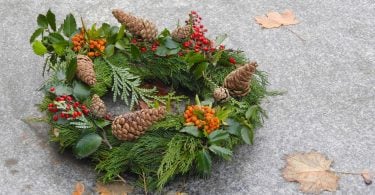 Imagem de uma llinda guirlanda de natal feita na cor verde, decorada com pinhas, flores na cor laranja e vermelho.