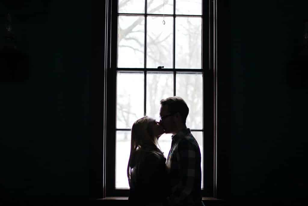 Homem e mulher se beijando em frente a uma janela.
