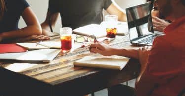 Pessoas reunidas na mesa com copos de chá, cadernos e notebook