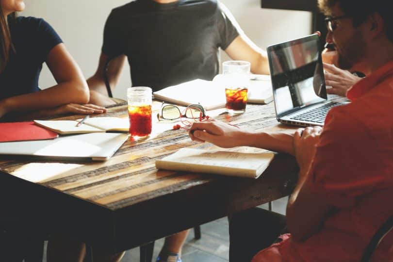 Pessoas reunidas na mesa com copos de chá, cadernos e notebook