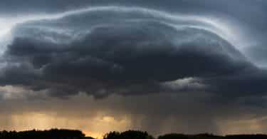 Imagem de um rodovia livre e ao lado um gramado bem verdinho. Ao fundo a formação de uma tempestade formada por um nuvem bem carregada e escura.