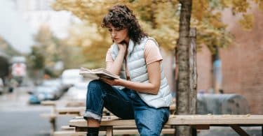 Mulher negra sentada numa mesa lendo um livro.