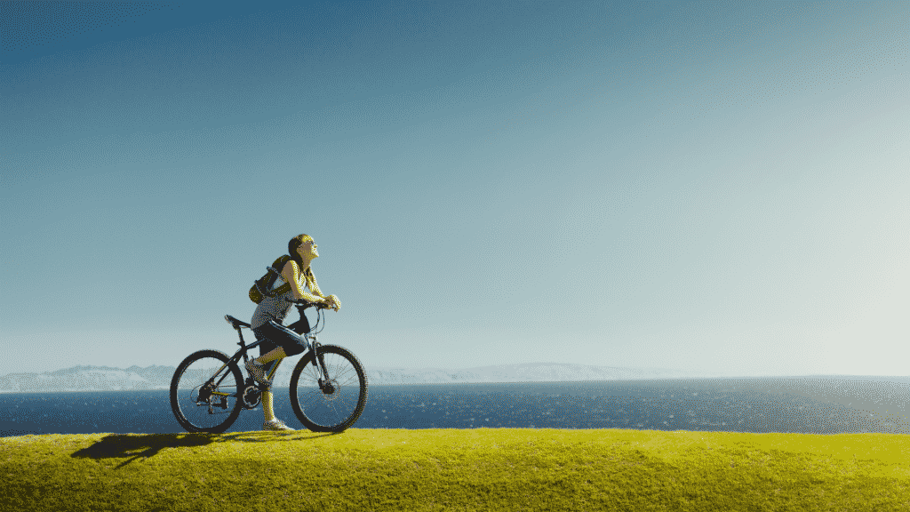 Mulher andando de bicicleta na beira do mar, olhando para o céu azul