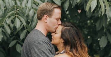 Homem branco beijando testa de mulher branca.