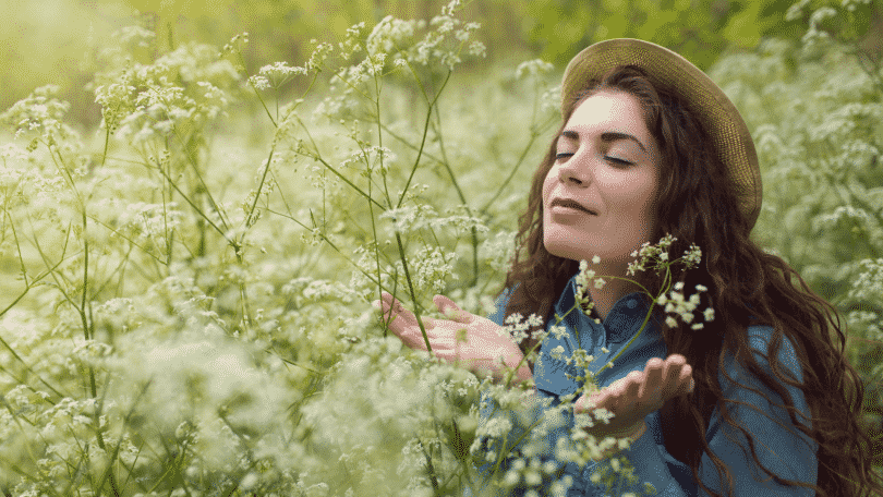 Mulher de olhos fechados em um campo, sentindo o aroma das flores