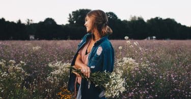 Mulher branca num campo de flores segurando ramo.