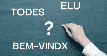 Uma mão com um giz escrevendo em uma lousa. Na lousa, um ponto de interrogação ao centro; à esquerda, "todes" e "bem-vindx" grafados. À direita "elu" grafado.