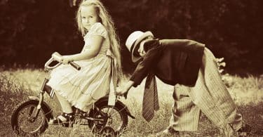 Menina e menino brancos brincando de bicicleta num campo.