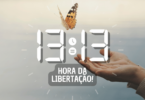 Hora igual 13:13 e texto "Hora da libertação!" aplicado por cima de foto de uma borboleta voando das mãos de uma mulher. Ao fundo, há um céu claro.