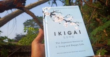 Mão humana segurando um livro cujo o escrito "Ikigai" está na capa.