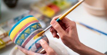 Mãos femininas pintando um vaso de argila.