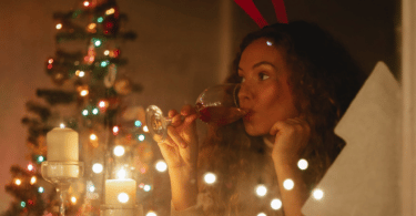 foto de uma mulher tomando uma taça devinho e uma árvore de natal no fundo da imagem