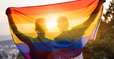 Casal abraçado levantando a bandeira gay