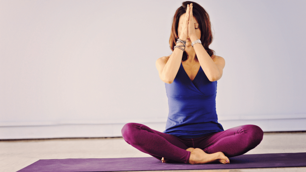 Mulher sentada em tapete de Yoga, com as mãos juntas. 