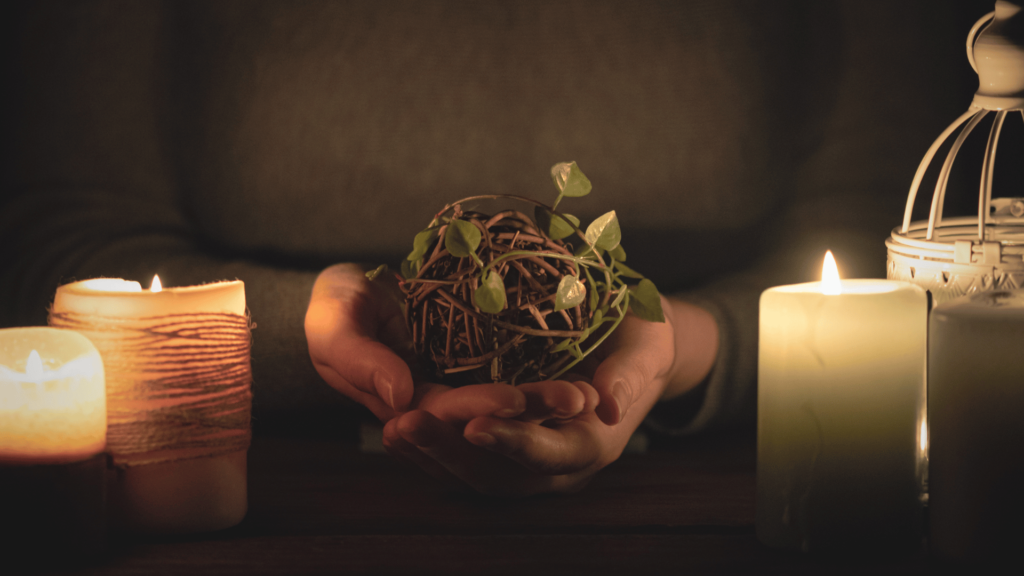 Bruxa segurando ervas medicinais, em mesa cheia de velas. 