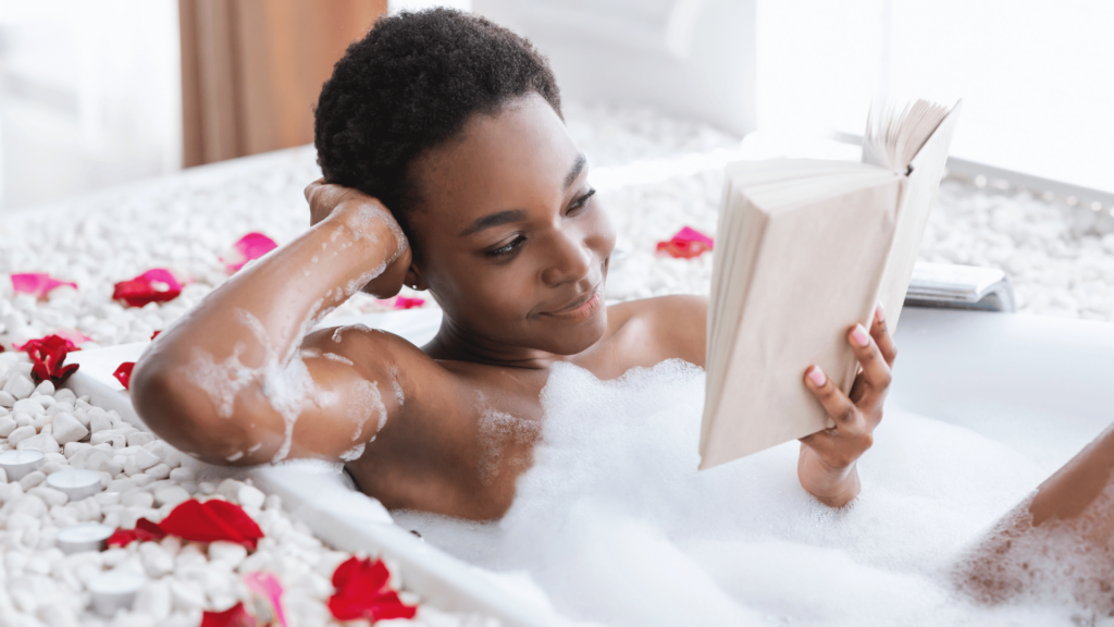 Mulher em banheira com espuma e pétalas de flores, segurando um livro. Conceito de autocuidado e descanso no fim de semana ou no tempo livre. 