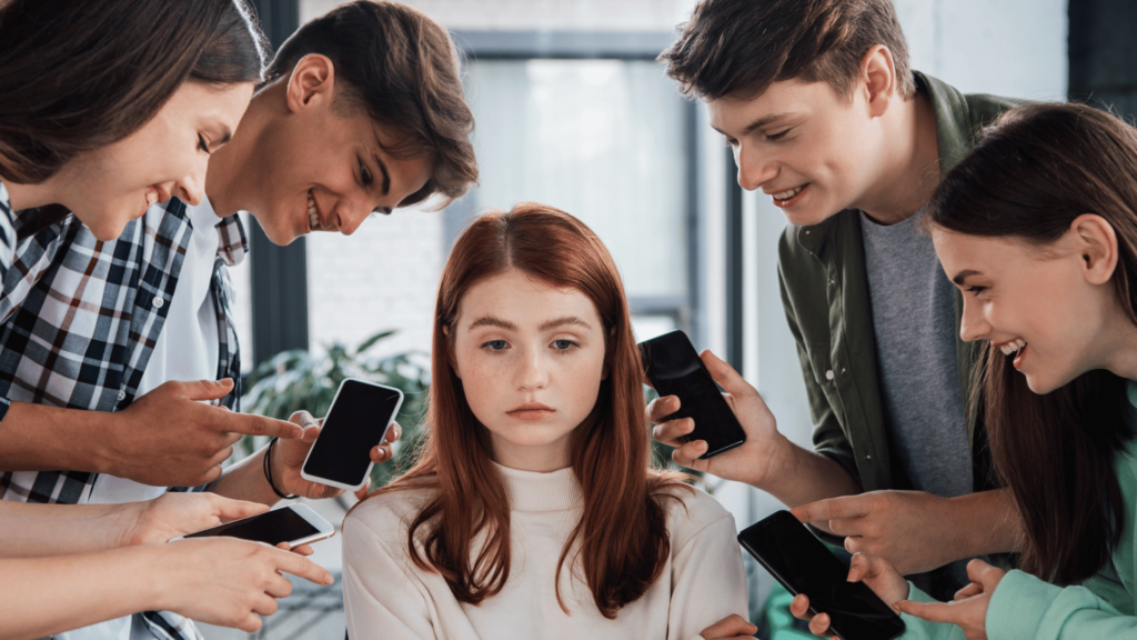 Adolescentes sorridentes apontando com os dedos para uma garota, enquanto fazem bullying e seguram seus smartphones. Conceito de cyberbullying. 