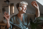 Mulher sênior feliz com fones de ouvido dançando em casa, relaxando e conceito de autocuidado.